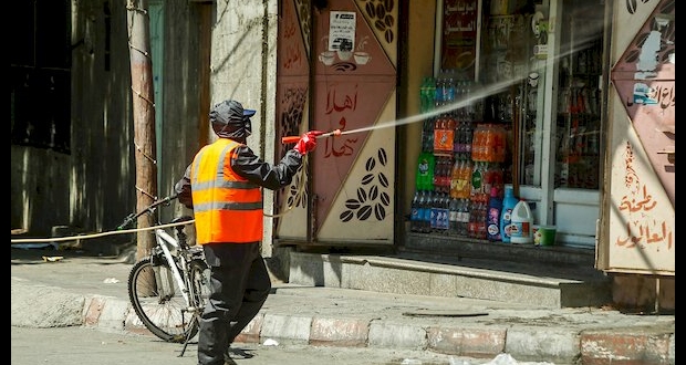 أحد الطواقم الصحية يقوم بتعقيم واجهة دكانة في مدينة غزة 